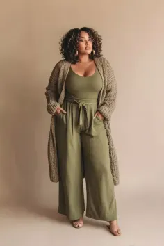 Woman with curly hair wearing an olive green jumpsuit and cardigan