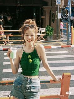 Woman in a green knit top and denim shorts smiling on a sunny street