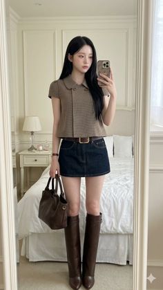 Woman with long black hair in a cropped top and denim skirt taking a mirror selfie