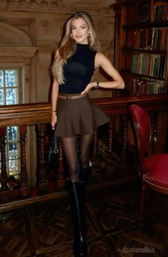 Woman in a black top and mini skirt with black tights and knee-high boots indoors