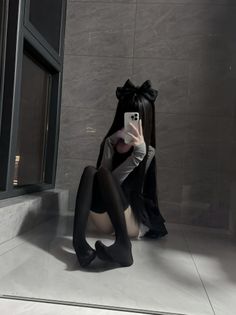 Person with long black hair and a bow taking a mirror selfie indoors