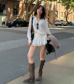 Woman in a white dress and long boots standing on a street