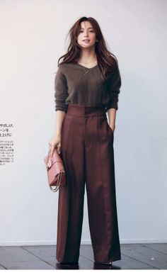 Woman with long hair wearing a brown sweater and wide-leg pants, holding a pink handbag