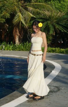 Woman in a long skirt and strapless top with a yellow flower in her hair by a pool