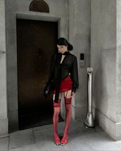 Woman in a red mini skirt and sheer top with red stockings standing indoors