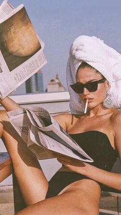 Woman in a towel wrap and sunglasses reading a newspaper outdoors