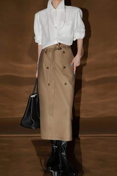 Person in a white shirt and belted midi skirt with black boots and handbag