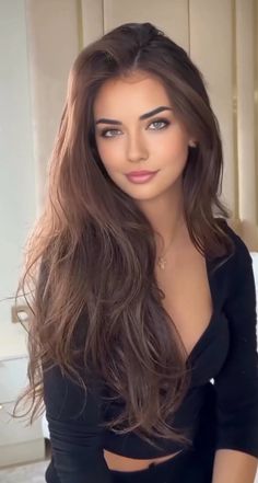 Woman with long brown hair wearing a black top with cleavage and a cross necklace