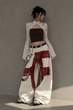 Woman in a lace bolero and wide leg pants against a gray wall