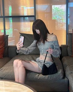 Woman in a plaid off-shoulder top and shorts taking a selfie indoors