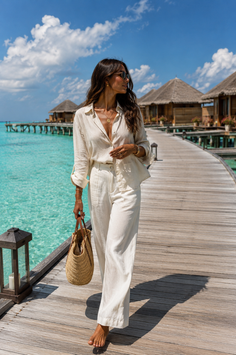 Woman in a white linen outfit walking barefoot on a wooden pier over turquoise water