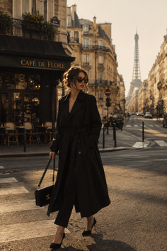 Woman in a black trench coat and sunglasses walking on a Paris street at golden hour