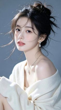 Woman with a messy bun wearing a white off-shoulder sweater and jewelry
