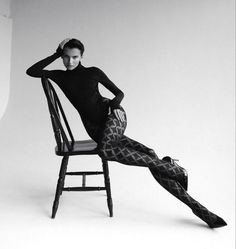 Woman in a black turtleneck bodysuit and patterned tights posing on a chair