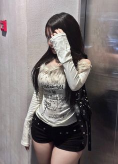 Woman with long black hair wearing a fur trim top and black shorts indoors