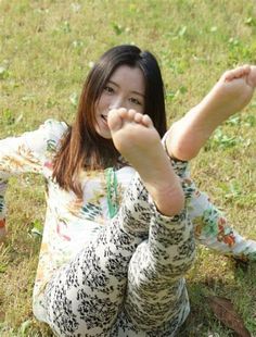 Woman with long hair lying on grass, smiling and showing her bare feet
