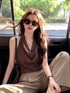 Woman with long hair and sunglasses in a polka dot top sitting in a car