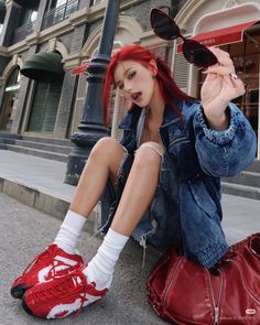 Woman with red hair in a denim jacket and ripped jeans sitting on a street