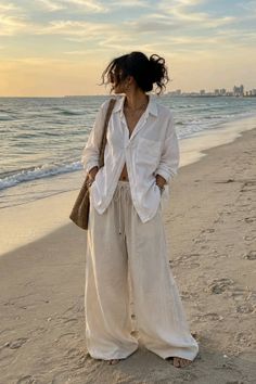 Woman in a white shirt and wide leg pants on a beach at golden hour