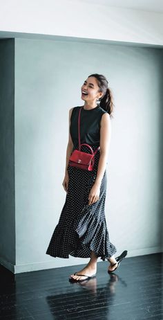 Woman in a black polka dot skirt and sleeveless top with a red handbag