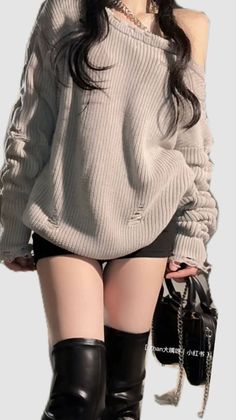 Woman in an oversized sweater, black shorts, and black boots holding a bag