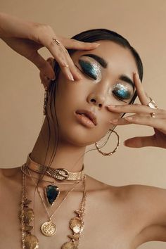 Woman with glitter eyeshadow and gold jewelry, hands near her face