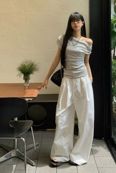 Woman with long black hair and glasses wearing a striped top and white wide-leg pants