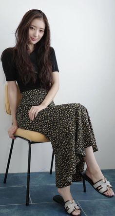 Woman with long hair wearing a black top and floral skirt, sitting indoors