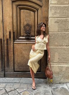 Woman in a satin top and skirt leaning against a wooden door