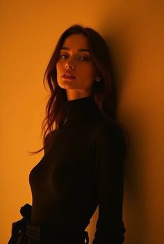 Woman with long hair wearing a black turtleneck against a warm-toned wall