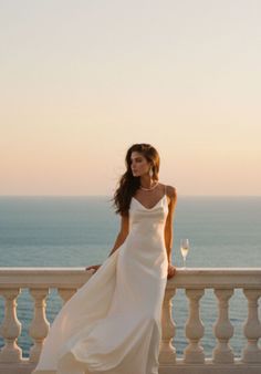 Woman in a white dress on a balcony overlooking the ocean at golden hour