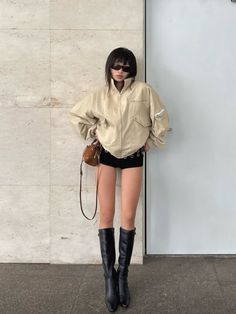 Woman in an oversized jacket, black shorts, and knee-high boots indoors