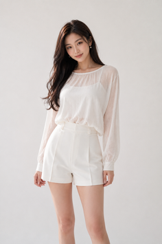 Woman with long dark hair wearing a white sheer blouse and white shorts