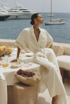 Woman in a white jumpsuit dining outdoors with an ocean view and yachts
