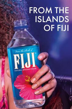 Hand holding a Fiji water bottle with a hibiscus flower label against a blue background