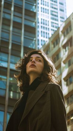 Woman with wavy brown hair looking up in a cityscape