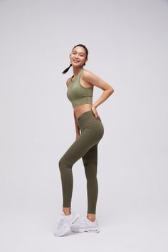 Woman in a green sports bra and leggings posing against a white background