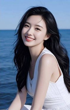 Smiling woman with long black hair in a white dress by the ocean