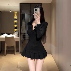 Woman in a black dress taking a mirror selfie indoors