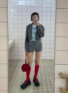Woman in a cropped blazer, knitted shorts, and red socks taking a mirror selfie