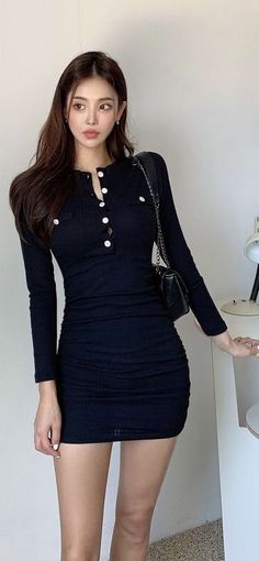 Woman in a black long-sleeve mini dress with white buttons posing indoors