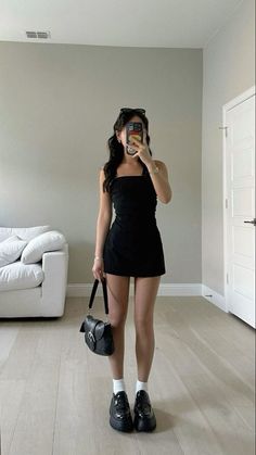 Woman in a black dress and platform loafers taking a mirror selfie indoors