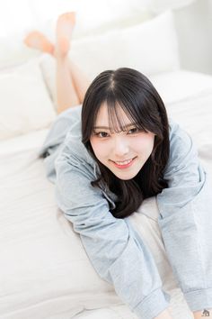 Woman with long black hair wearing a grey hoodie, lying on a bed and smiling