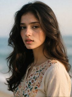 Woman with long dark hair wearing an embroidered top at the beach