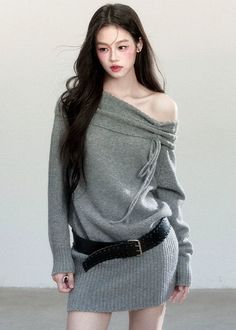 Woman with long dark hair wearing an off-shoulder gray sweater and black belt