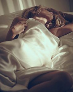 Woman with blonde hair lying in bed under a sheet with soft lighting