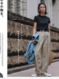 Woman in a black t-shirt and khaki pants holding a denim jacket and straw bag