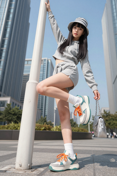 Woman in a grey hoodie and shorts posing with a bucket hat in a cityscape