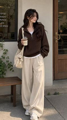 Woman in a brown sweater and wide leg pants holding a drink outdoors