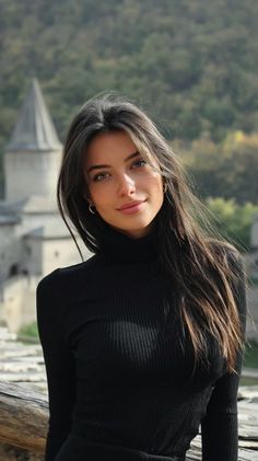 Woman with long dark hair wearing a black turtleneck outdoors with a castle in the background